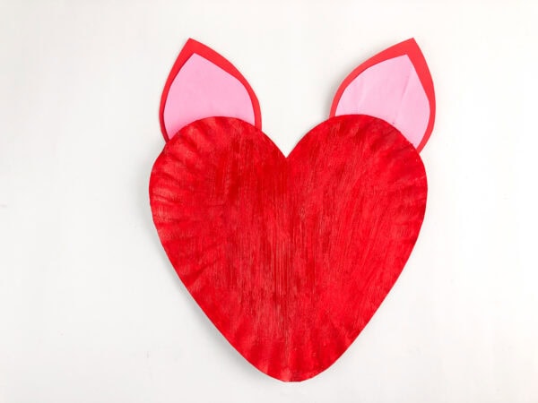 Red painted heart paper plate with unicorn ears attached.
