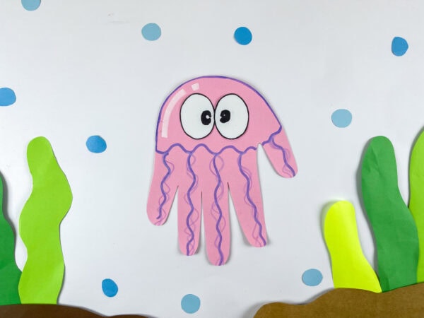 Finished pink jellyfish handprint craft displayed in an underwater scene