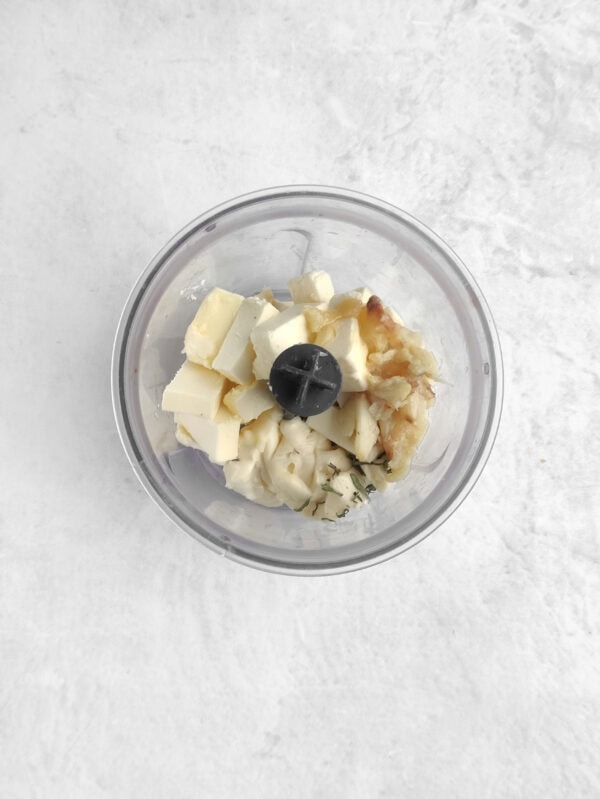 Chopped brie, butter, garlic, and herbs in a food processor bowl.