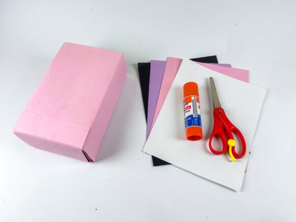 Craft supplies with pink box, paper, glue stick, and scissors