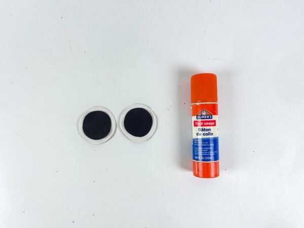 Googly eyes beside an orange glue stick