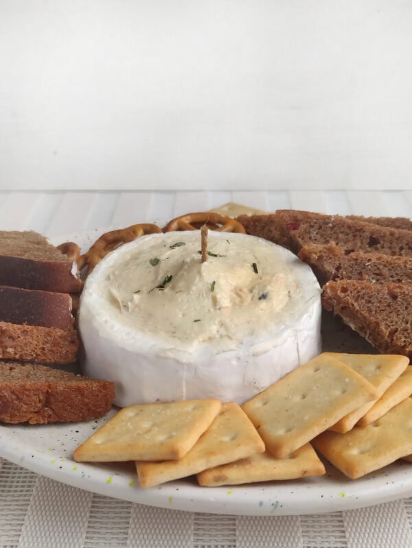 Brie cheese candle on a plate surrounded by bread slices, pretzels, and crackers.