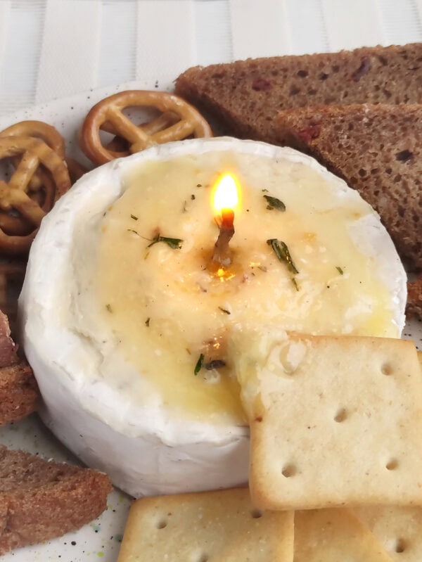 Lit brie cheese candle on a plate surrounded by crackers and bread.
