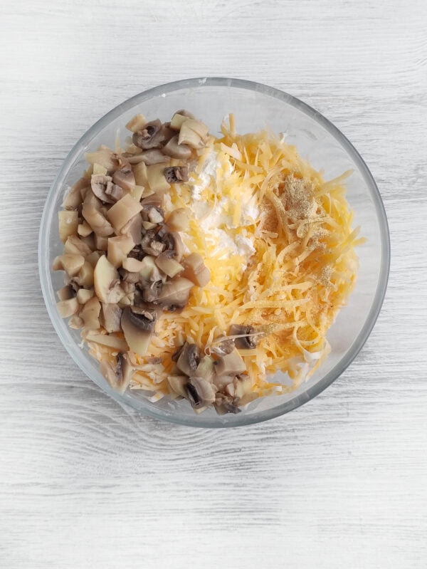 Mixing cream cheese with shredded cheese, chopped mushrooms, and seasoning in a bowl