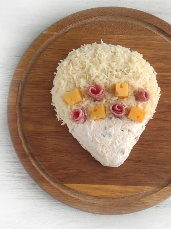 Cheese spread hedgehog covered with shredded cheese and decorated with salami and cheese cubes