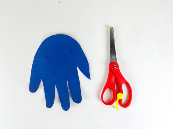 Blue handprint cutout placed beside scissors for dinosaur body base