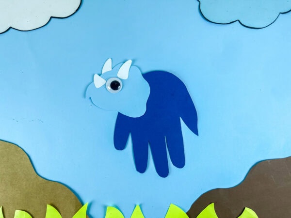 Finished triceratops handprint craft displayed on sky background scene