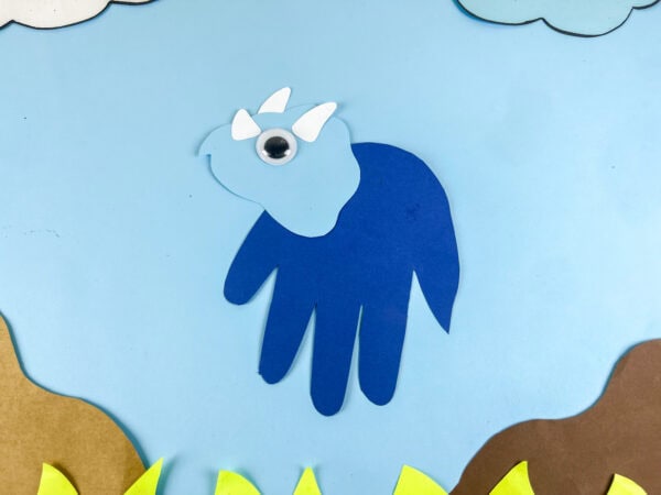 Triceratops handprint craft centered with grass and sky background