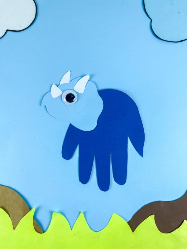 Full triceratops handprint craft on sky background with clouds and grass