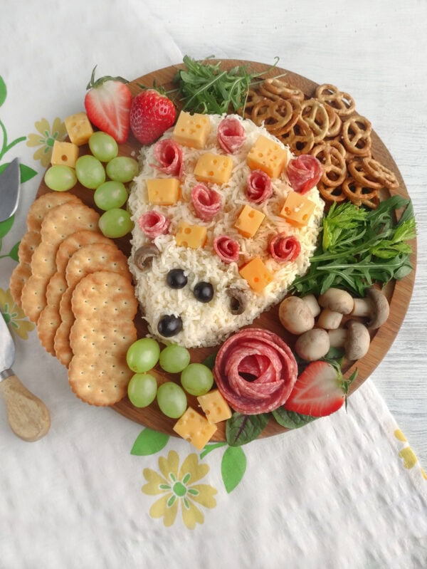 Overhead view of hedgehog charcuterie board with crackers, grapes, strawberries, pretzels, mushrooms, and cheese cubes