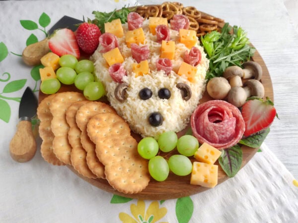 Front view of hedgehog cheese spread charcuterie board with crackers, grapes, salami rose, and pretzels