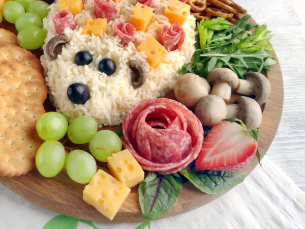 Close-up of hedgehog cheese spread with salami roses, cheese cubes, grapes, and mushrooms