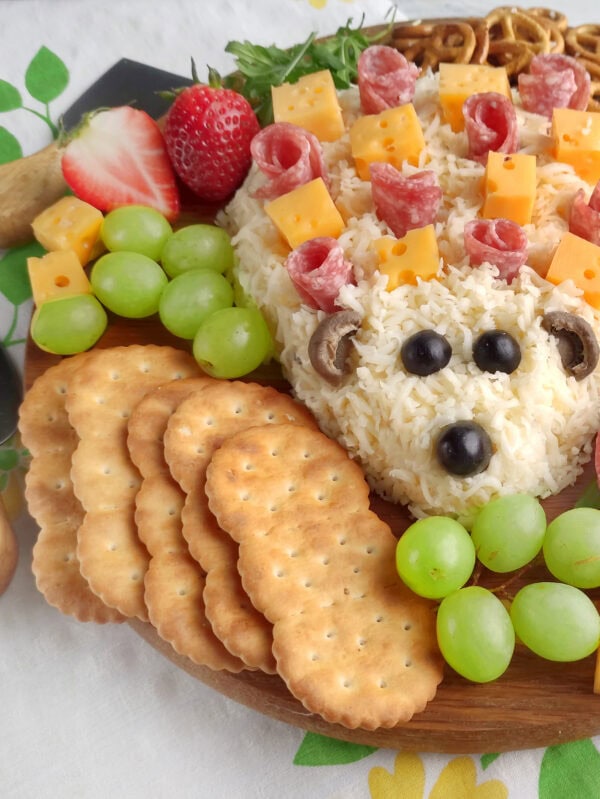 Close-up of hedgehog cheese spread face with crackers, grapes, strawberries, and cheese cubes