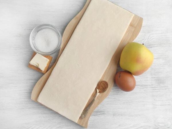 Puff pastry sheet with egg, sugar, and apple on board