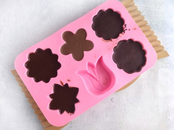 Filled silicone mold with flower-shaped chocolate pieces setting