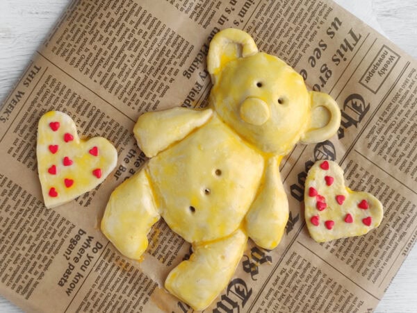 Egg wash applied to teddy bear pastry with heart shapes
