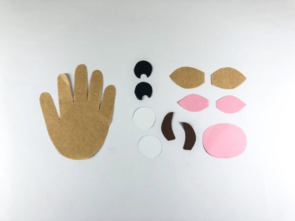 Cut paper pieces arranged for cow handprint craft assembly