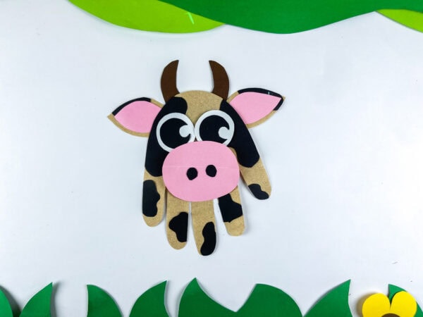 Finished cow handprint craft on white background with grass border