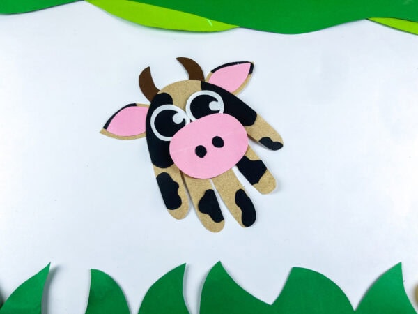 Cow handprint craft displayed on white background with paper grass
