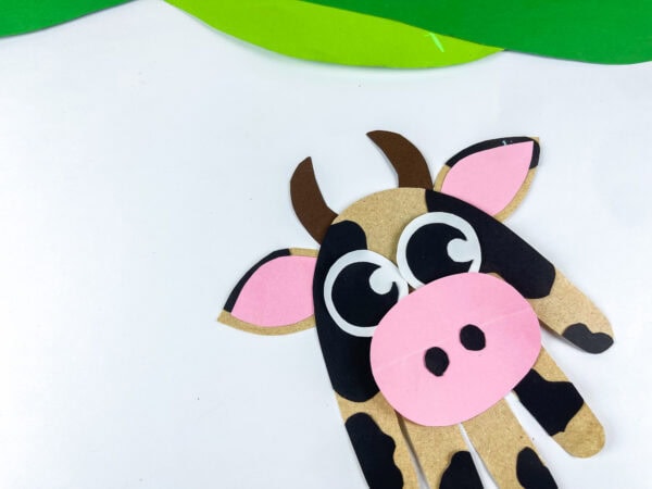 Cow handprint craft placed between paper grass and flowers