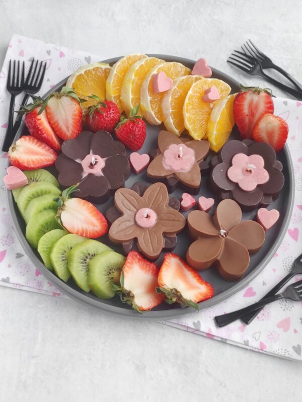 Chocolate flower candles arranged with sliced fruit on platter