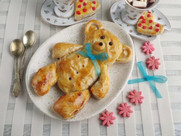 Teddy bear pastry plated with ribbon and tea cups
