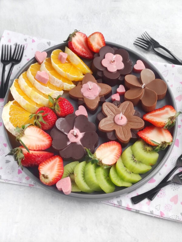 Close-up chocolate flower candles with strawberries, oranges, and kiwi on tray