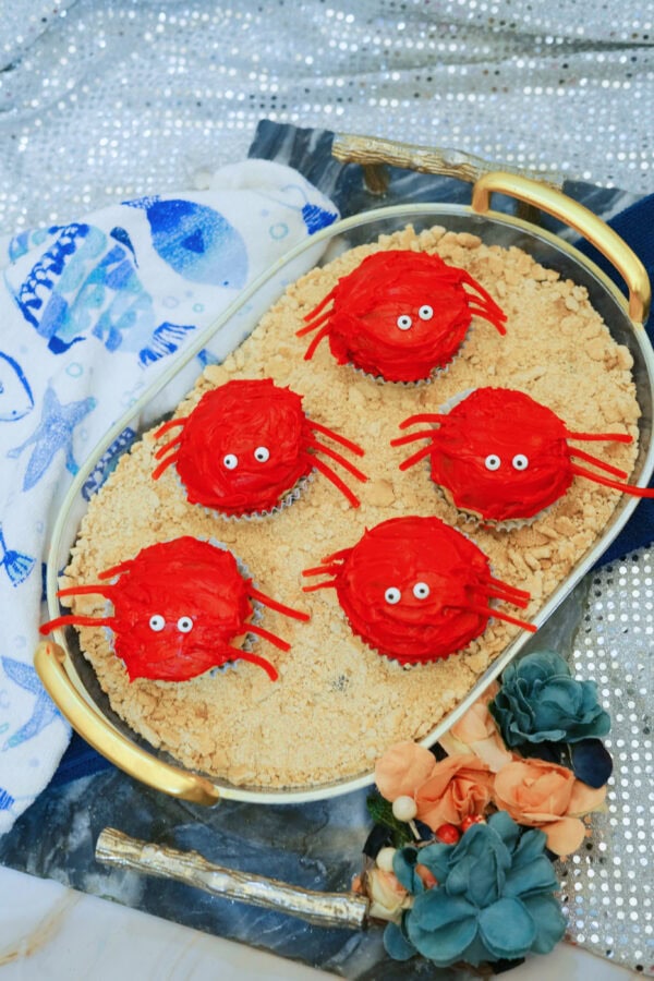 Five red crab cupcakes arranged on graham cracker crumbs in oval tray