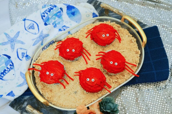 Crab cupcakes displayed on oval tray with beach-themed cloth