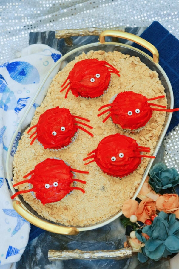 Red crab cupcakes arranged on graham cracker sand in oval tray