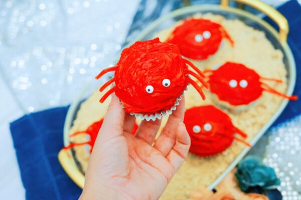 Hand holding red crab cupcake with candy eyes and licorice legs

