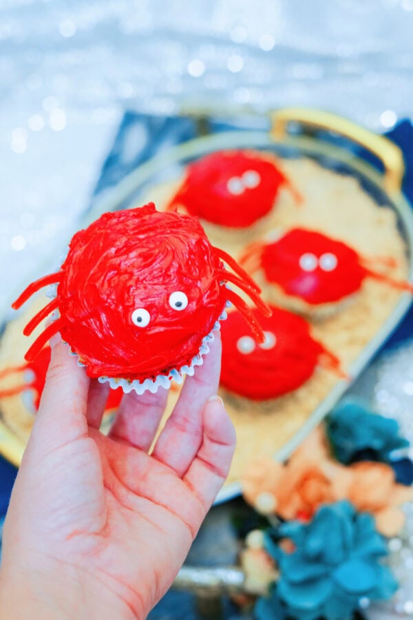 Hand holding red crab cupcake with candy eyes and licorice legs