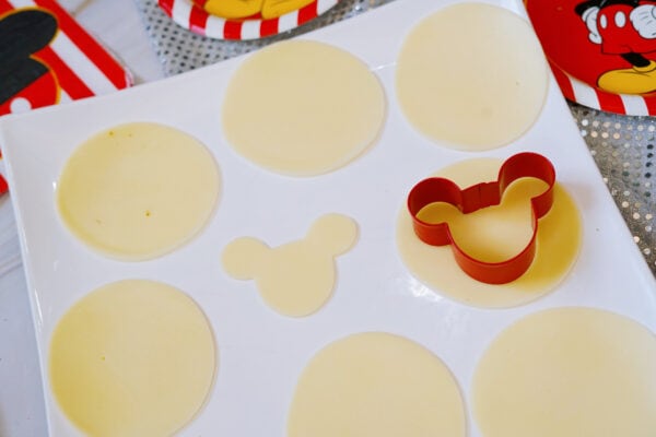 Mickey-shaped cheese cutouts with cookie cutter on plate
