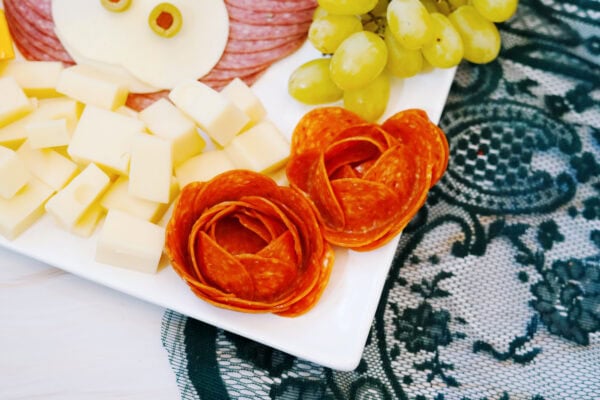 Pepperoni roses beside cheese cubes and grapes