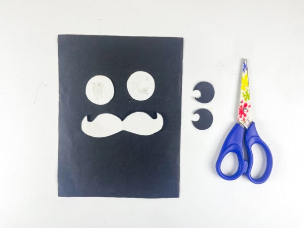 Paper eyes and mustache cutouts with scissors