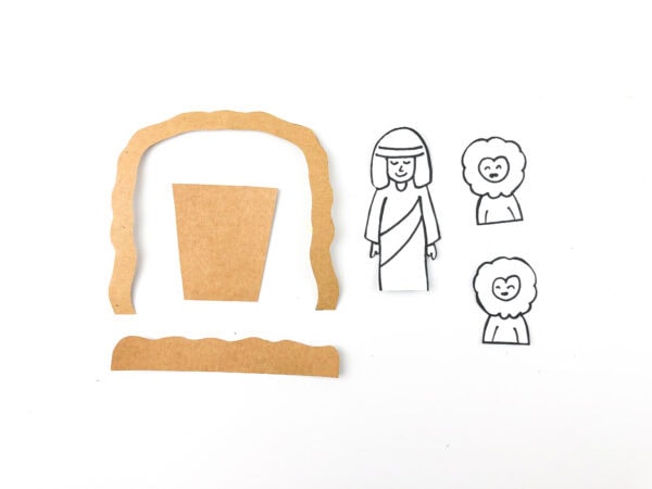 Cut-out cardboard cave arch pieces beside black-and-white printable cutouts of Daniel and two lions.