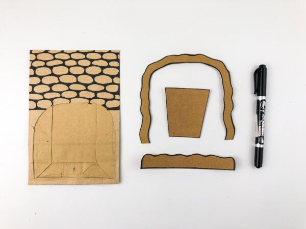 Cut paper bag pieces with stone-pattern drawing, cave arch, and a marker.