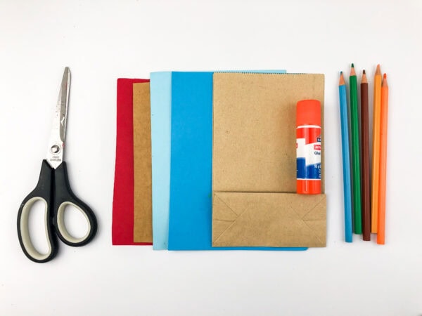 Craft supplies including a paper bag, colored paper, scissors, glue stick, and colored pencils.