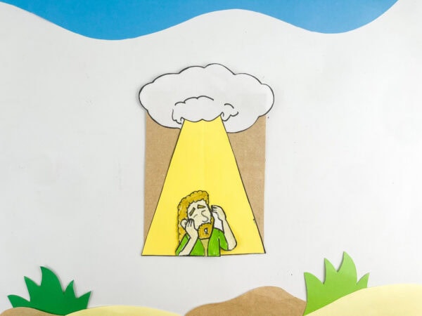 Completed paper bag craft showing Saul under a light beam, displayed against a blue and sand-colored background.