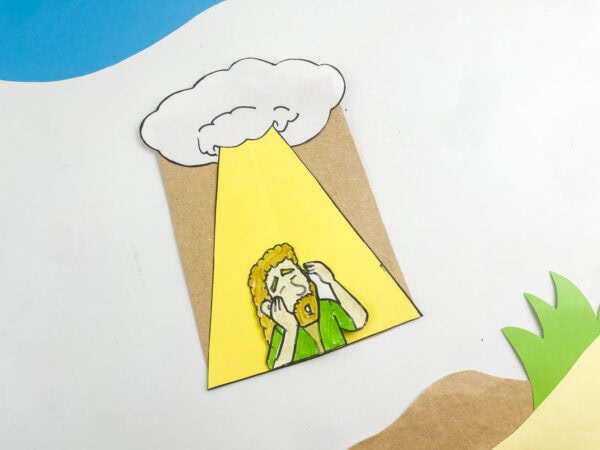 Completed paper bag craft of Saul's conversion, displayed alongside paper cutout grass and sky elements.