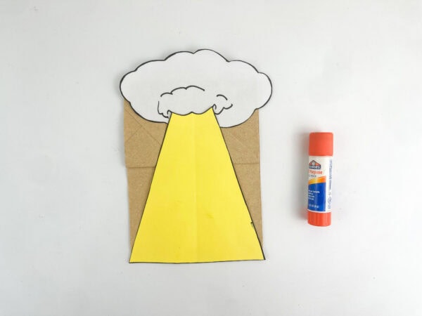 The paper cloud and yellow beam glued onto a brown paper bag next to a glue stick.