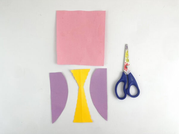 Pink, purple, and yellow paper pieces cut into dress shapes next to scissors