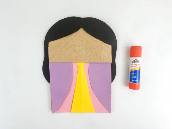 Dress shape glued onto the paper bag with hair, next to a glue stick