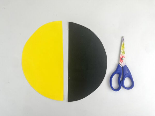 Two paper semicircles—one yellow and one black—placed side by side next to a pair of scissors.