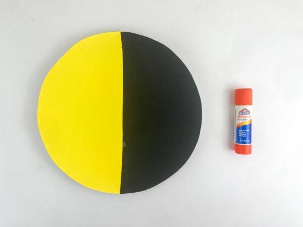 A yellow and black paper circle glued together, sitting next to an orange glue stick.