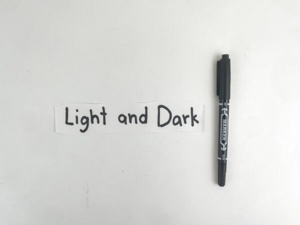 A white paper strip with the handwritten words "Light and Dark" next to a black marker.