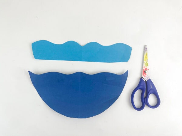 Two wavy cutouts of light blue and dark blue construction paper next to a pair of scissors.