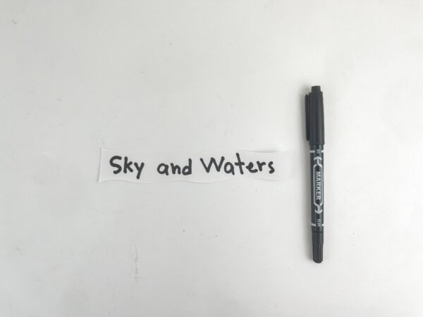 A strip of white paper with the handwritten text "Sky and Waters" next to a black marker.
