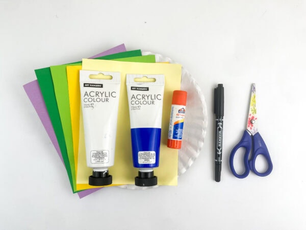 Craft supplies including tubes of white and blue acrylic paint, a glue stick, a black marker, scissors, a paper plate, and colored sheets of paper.