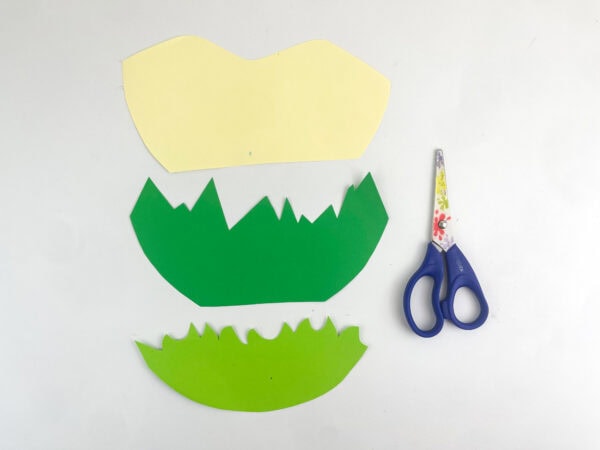 Three cut-out construction paper shapes representing rolling hills and grass layers next to a pair of scissors.